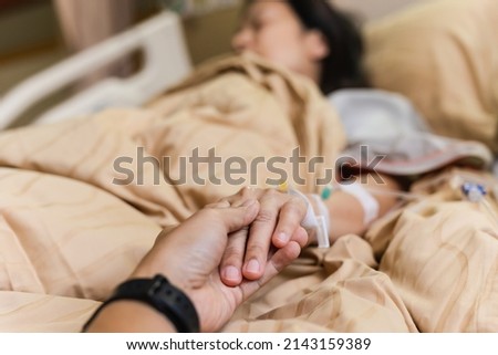 Husband hand holding his wife hand on bed in hospital room