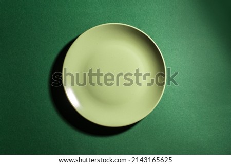 Green empty plate on dark green background, top view, copy space. Cooking and eating healthy food concept, meal design mock up.