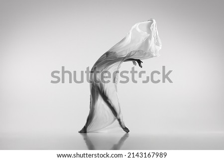 Liberty. Black and white portrait of graceful ballerina dancing with fabric, cloth isolated on grey studio background. Grace, art, beauty, contemp dance concept. Weightless, flexible actress Royalty-Free Stock Photo #2143167989