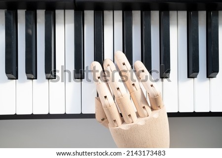 Wooden hand of a mannequin plays the piano, in natural light from the window. Top view. 