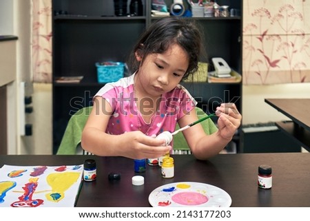 Cute adorable baby girl learning drawing and painting with poster colors at home. Healthy happy daughter experimenting with colors; covid-19,online learning,physical distancing concepts.