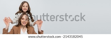 woman holding hands of cheerful daughter isolated on grey, banner