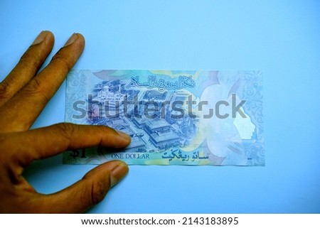 1 BND, One Brunei dollar, money concept pointed by left hand businessman isolated on blue background                     