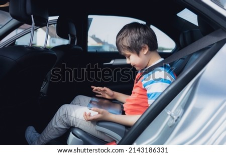 Cinematic portrait Happy young boy using a tablet computer while sitting in the back passenger seat with a safety belt, Child typing on smart pad,School kid traveling to school by car.Back to school