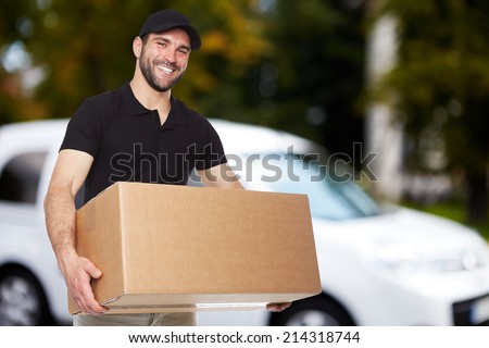 Smiling delivery man holding a paper box Royalty-Free Stock Photo #214318744
