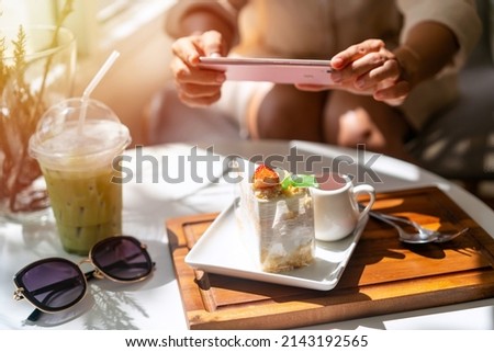 Young woman taking photo of dessert with smart phone for social media in restaurant while traveling