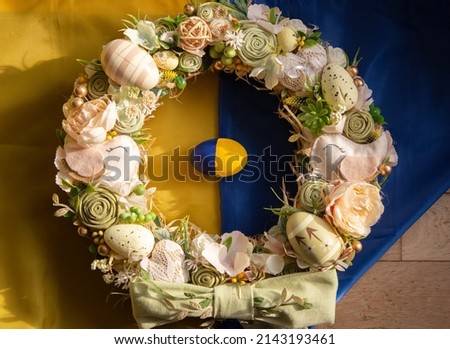 Easter festive decorative wreath lies on the Ukrainian flag and an egg painted in yellow and blue colors. Easter concept. Support Ukraine
