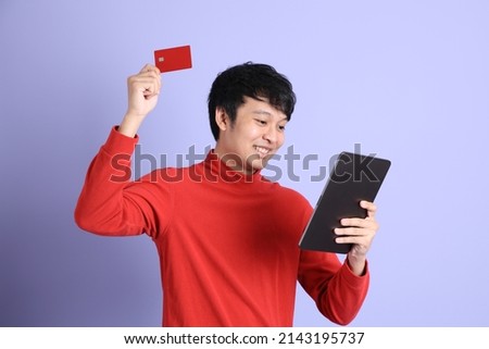 The young adult southeast Asian man with red long sleeve shirt standing on the light green background.