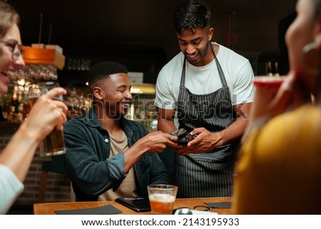 diverse friends out for dinner paying with cellular device  Royalty-Free Stock Photo #2143195933