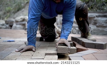 Closeup of hand putting brick paver into place in a hardscaping project. Royalty-Free Stock Photo #2143211125