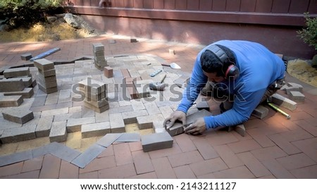 A brick paver artisan sets bricks into position for cutting for a two tone hardscaping design. Royalty-Free Stock Photo #2143211127
