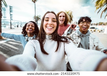 Young people taking selfie photo with smart mobile phone outside - Multicultural friends running on city street enjoying freedom - Happy students celebrating summer holidays 