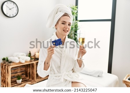 Young caucasian woman relaxed drinking champagne holding credit card at beauty center.