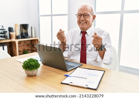 Senior man working at the office using computer laptop doing money gesture with hands, asking for salary payment, millionaire business 