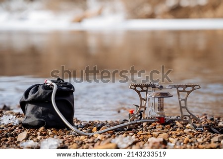 A tourist burner stands on rocks against the background of the river, a gas burner with a hose and a gas cylinder, the concept of camping equipment for a hike. High quality photo