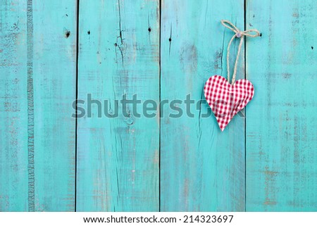 Red checkered country heart hanging from rope on antique teal blue rustic weathered wood background