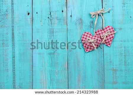 Two plaid red hearts hanging from rope on antique teal blue distressed wood door