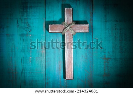 Spotlight on worn wooden cross hanging on antique teal blue wood background