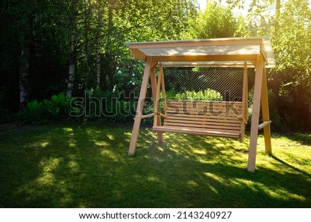 Wooden summer swing on the green grass in the garden. Garden decoration. Landscape design.Summer vacation in the country. Royalty-Free Stock Photo #2143240927