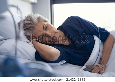 Sad senior woman lying on side on hospital bed. Depressed old patient lying on gurney at clinic with iv drip on hand. Elderly lonely woman with terminal illness resting at hospital ward. Royalty-Free Stock Photo #2143243895