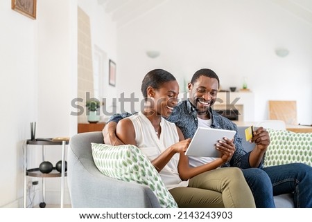 Happy african american wife doing shopping online while using digital tablet and credit card at home with husband. Middle aged black couple making an online purchase using debit card on digital tablet