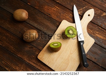 One kiwi fruit cut in halves and two whole kiwi fruit with a knife on wooden table and background.