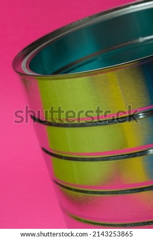 An empty aluminum can tipped on a diagonal, highlighted with vibrant colors on a bright pink background.
