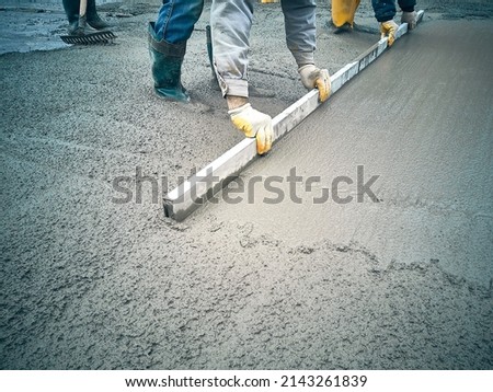Construction worker uses trowel to level cement mortar screed. Concrete works on construction site. Cast-in-place work using trowels.  Royalty-Free Stock Photo #2143261839