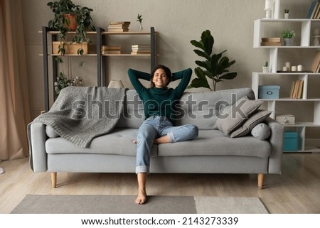 Sweet idleness. Lazy young hispanic lady sit in relaxed pose on big comfy sofa at living room interior breath air dream imagine. Successful female new flat apartment buyer rest at home feel pleasure Royalty-Free Stock Photo #2143273339