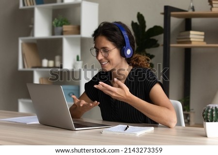 Confident hispanic female interpreter work from home office sit at desk in headset talk look on laptop screen translate online event. Young lady participate at web conference negotiate using pc webcam