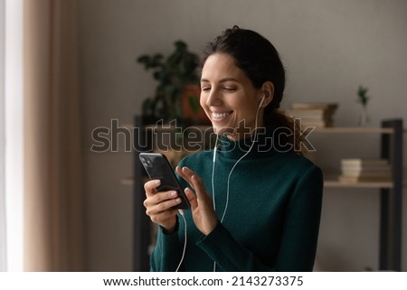 Modern leisure time. Joyful millennial latina female in portable wired headset text on phone chat online using wifi choose song from web playlist. Smiling young lady relax using smartphone headphones
