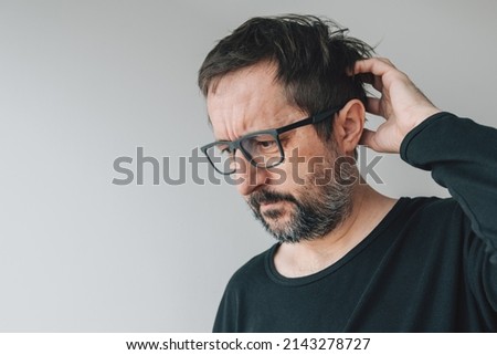 Forgetfulness - forgetful mid-adult man with eyeglasses indoors, trying to remember Royalty-Free Stock Photo #2143278727