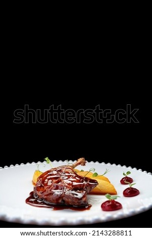 Duck leg with pear in caramel, on a white plate, on a dark background