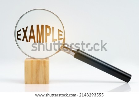 Economic concept. On a white surface there is a cube and a magnifying glass inside which is the inscription - EXAMPLE Royalty-Free Stock Photo #2143293555