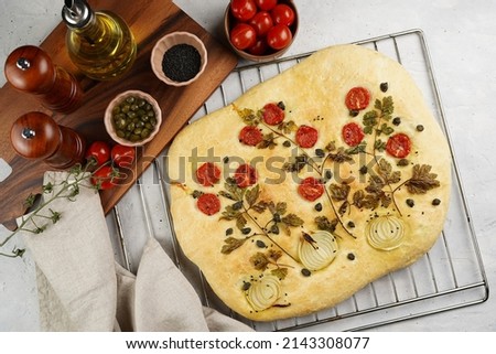 Floral painting focaccia, italian garden flatbread art with parsley, tomatoes, onions, sesame seeds and capers on light grey background