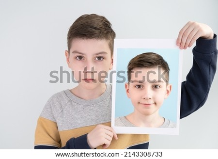 A boy with a sad face holds his photo with a cheerful face in his hands. Social concept.