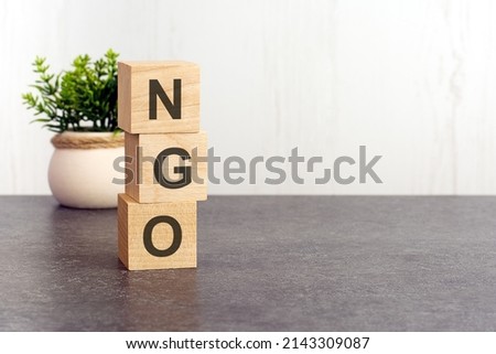 letters of the alphabet of NGO on wooden cubes, green plant, white background. NGO - short for Non-Governmental Organization