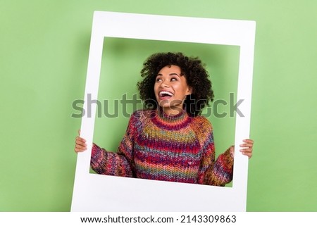 Photo of funky young curly hairstyle lady hold frame look ad wear red sweater isolated on green color background