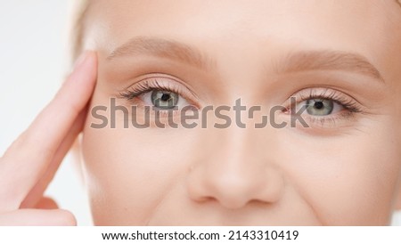 Extreme close-up shot of Caucasian blond female model lifts her eye with her fingers on white background | Droopy eyelids treatment concept Royalty-Free Stock Photo #2143310419