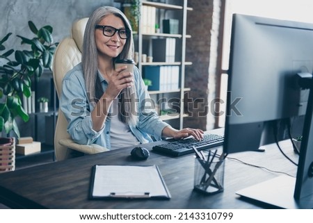 Photo of joyful smile lady ceo pensioner retired sit table drink takeaway mug latte use device monitor prepare project in workspace