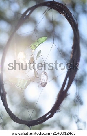 a dream catcher made of a branch, threads and glass hanging in nature among the trees, a photograph against the light with bright sun glare