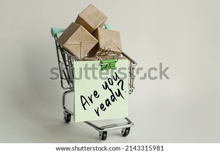 A sticky note attached to a decorative grocery cart along with small packaged letterboxes. Lettering content has implications for shops, sales, and marketing. Side view on white isolated background.