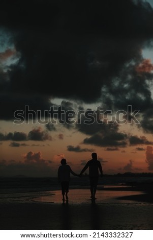 Lovely couple walking on the sandy beach during the colorful sunrise early morning cloudy silhouette