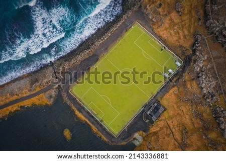 Aerial view of an old football field with scenic cliffs in the background located on the coast near the village of Eidi in Faroe Islands, Denmark. November 2021