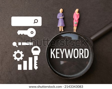 Miniature people,magnifying glass and icon with text KEYWORD on black background.
