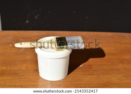 Selective Focus of A Flat Paint Brush on A White Paint Bucket Isolated with Black And Wooden Background. Soft Focus and Over Exposure in Photo due to Lighting from Sun