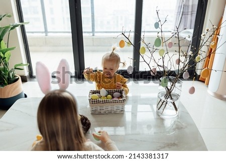 happy caucasian toddler girl eight years old and her baby sister one year old at home in living room with colored easter eggs. Stay home during Coronavirus covid-19 pandemic