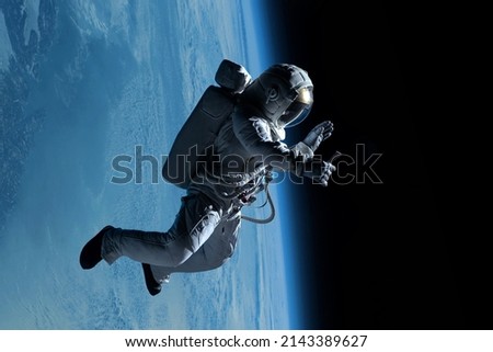Female astronaut having a video call on her phone while performing spacewalk in deep space, Earth in the background Royalty-Free Stock Photo #2143389627