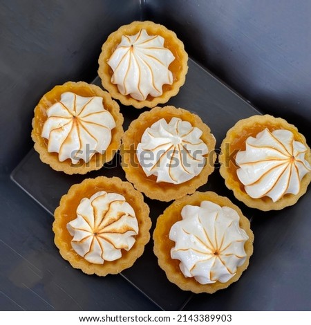 Top view on lemon meringue mini tarts in a black tray.