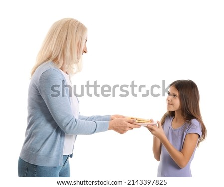 Mature woman giving plate with cookies to her little granddaughter on white background